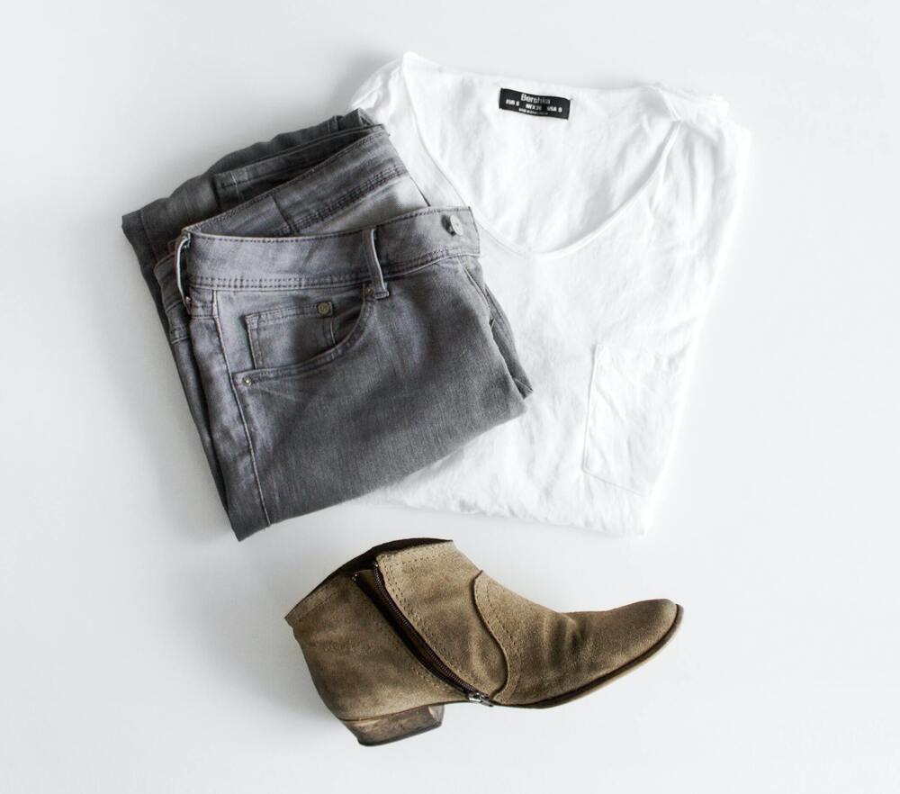 A folded pair of jeans, white t-shirt and brown heeled boot over a gray background that represents extreme minimalism and an extreme minimalist wardrobe