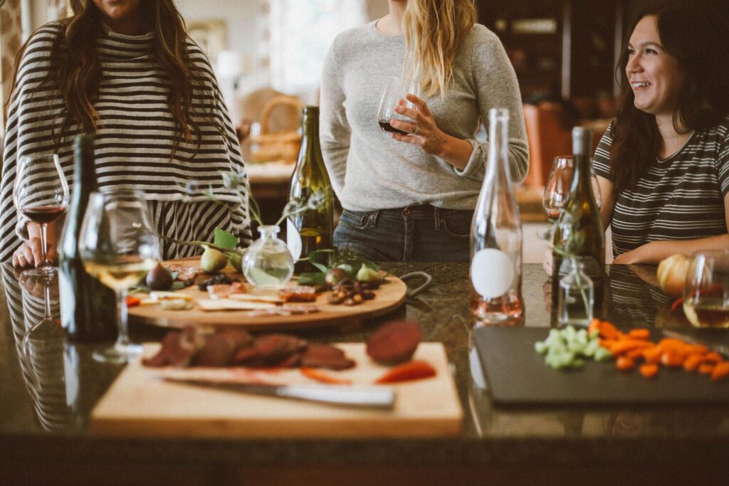 Three women sitting around a dining table eating charcuterie and drinking wine. This symbolizes the importance of finding free alternatives to activities you enjoy when starting a no-buy year. 
