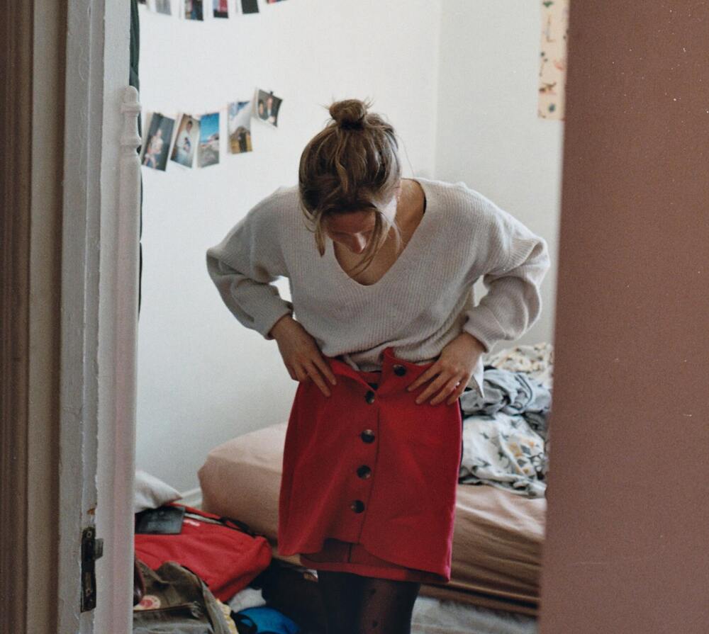 A girl trying on a red skirt in her bedroom