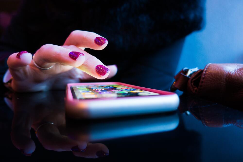 a hand with red fingernail polish scrolling on a phone