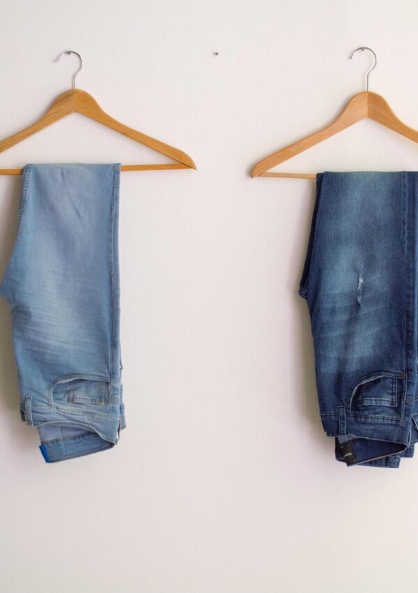 Two pair of jeans hanging on clothing racks in a minimalist capsule wardrobe