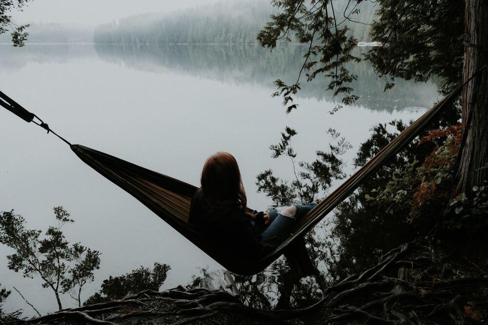 A woman sitting in a hammock overlooking the water that symbolizes minimalism 