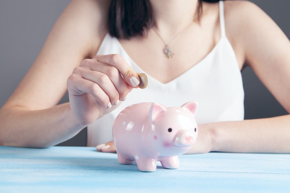a girl putting money into her piggy bank that represents how to budget money 