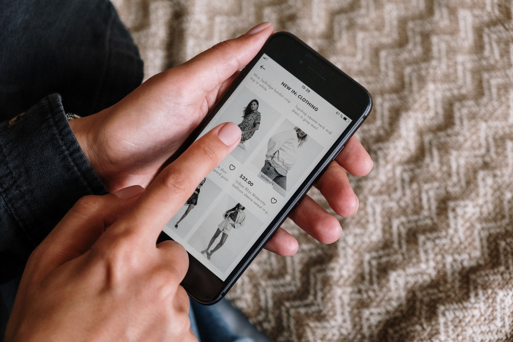 A close up image of someone's hand scrolling through an online clothing store on their phone but the phone is grayscale mode. 