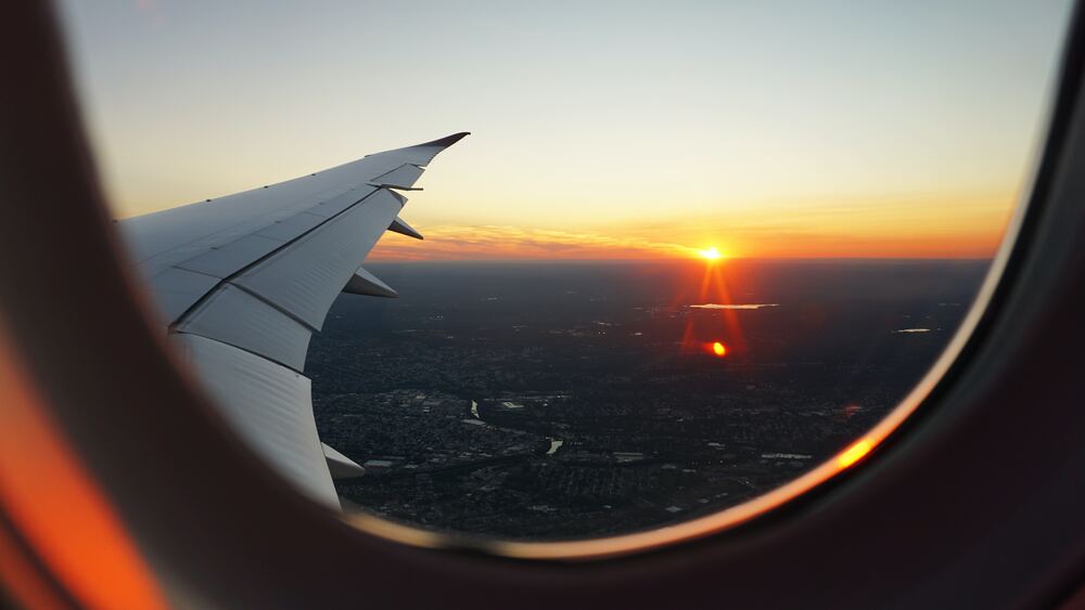 An image of an airplane window with a sunset in the horizon which represents accounting for transportation to the destination within your travel budget