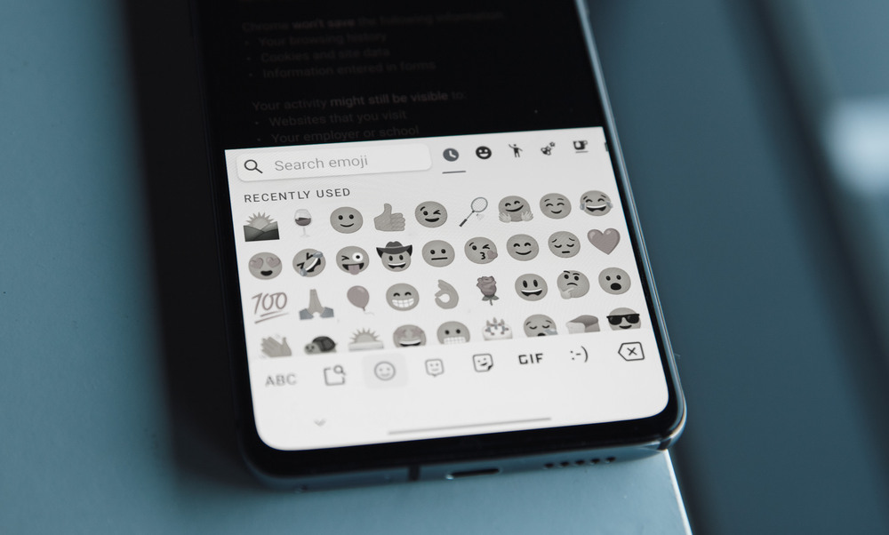 A phone in grayscale mode shows emojis that are black and white in color
