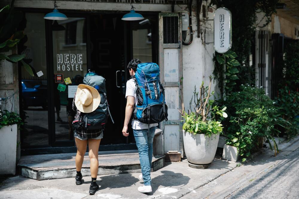 Two people wearing backpacking backpacks walking into a hostel. This image represents planning accommodations  in your travel budget