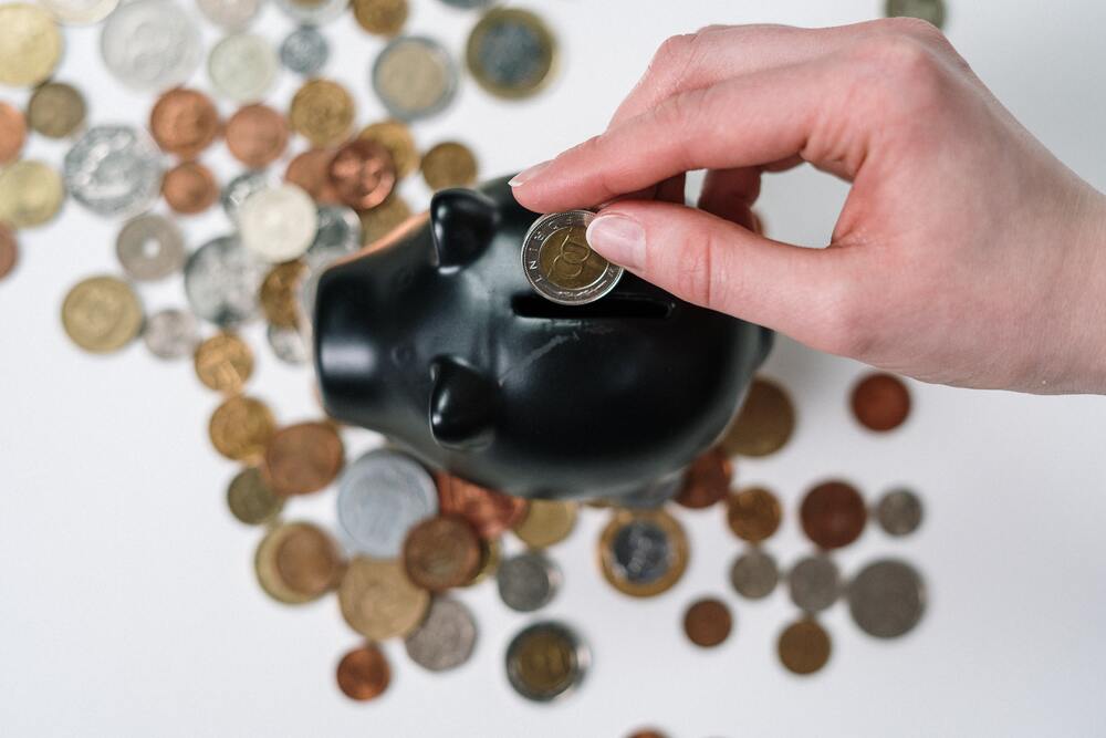 An image of a hand putting coins into a black piggy bank