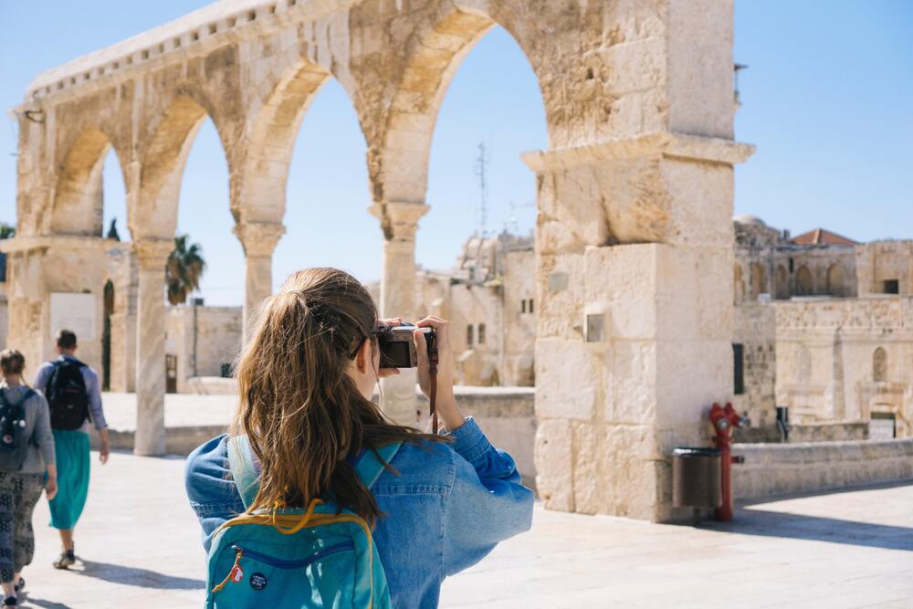 A girl taking a photo of an ancient ruin which represents the types of attractions you may plan when developing your travel budget