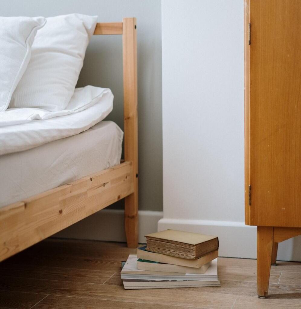 A corner of a bed and books piled up on the floor beside it that represent extreme minimalism 