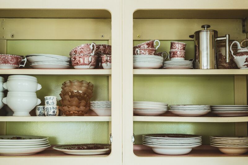 Stacks of dishes including teacups, plates and bowls in a green kitchen cabinet