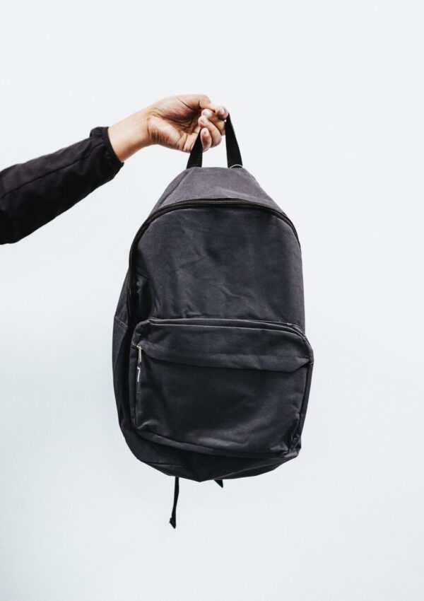 an image of an arm holding a black backpack in front of a gray background that represents extreme minimalism