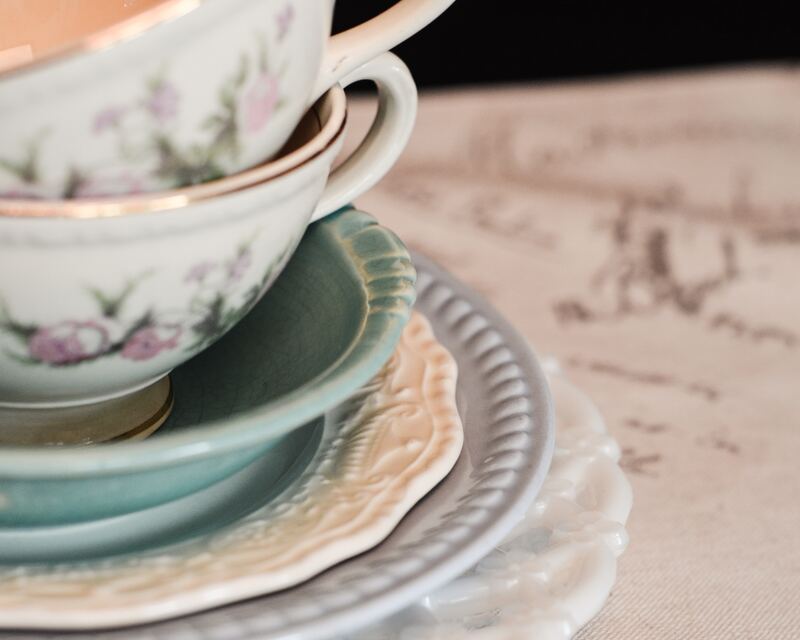 A stack of dishes including two floral teacups and some pastel colored plates