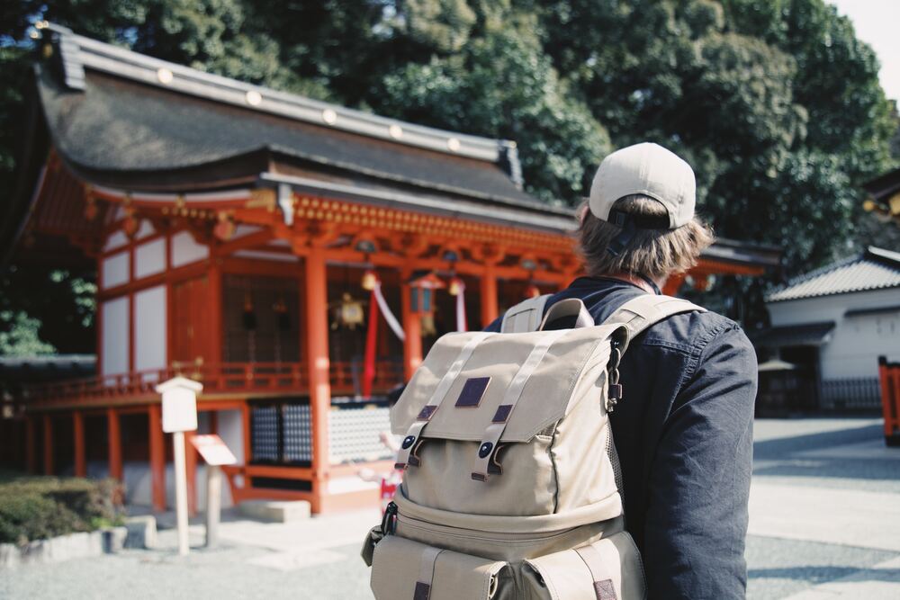 A person wearing a backpack in front of a Japanese style building that represents extreme minimalism travel
