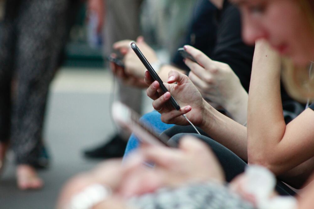 A close up image of people sitting around on their cell phones that represents cell phone addiction