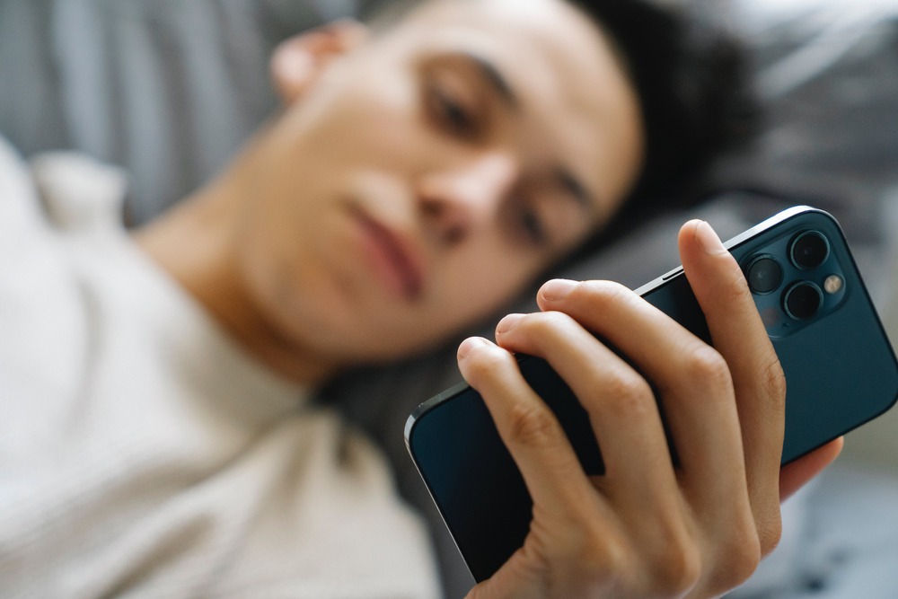 A person holding their phone in bed. This image symbolizes the need for a digital detox
