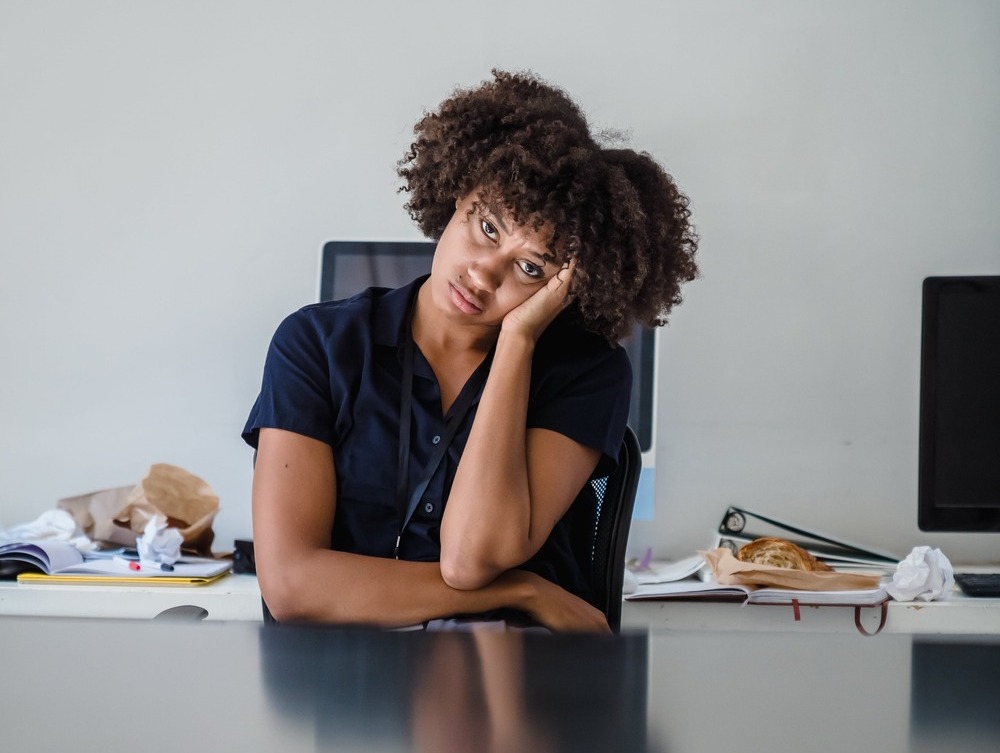 A woman looking sad while sitting at her desk with her head in her hand because her work feels meaningless