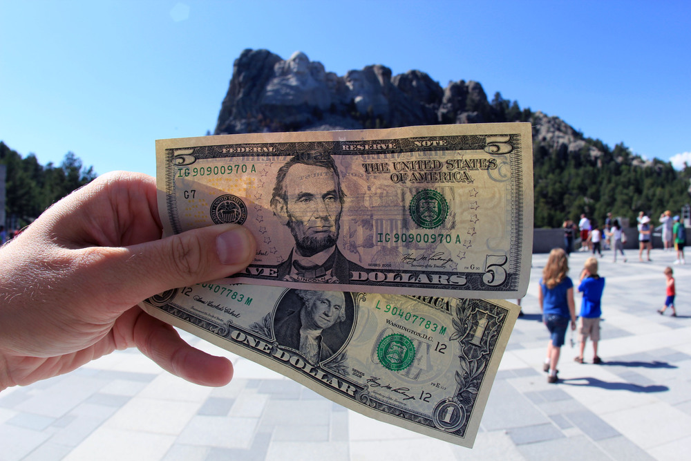 A person holding up a $5 and $1 bill while on vacation. This image symbolizes making passive income