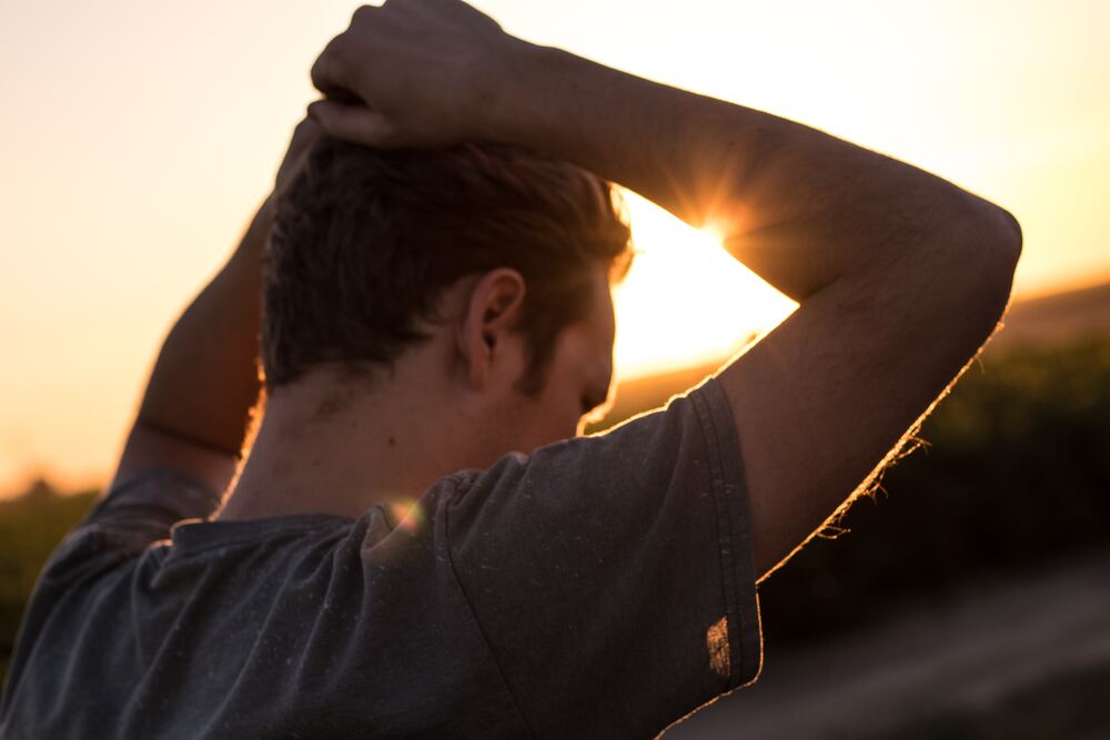 A man holding his arms above his head in front of a sunrise. This image represents feeling overwhelmed by minimalism