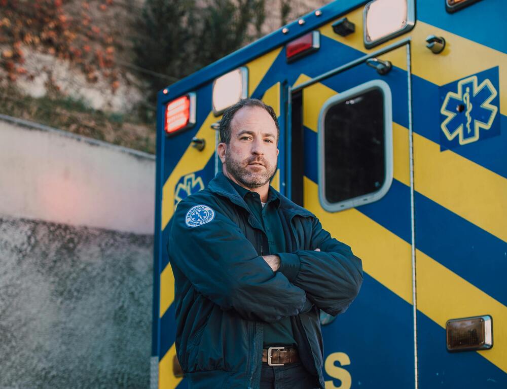 An EMT standing in front of an emergency vehicle with his arms crossed