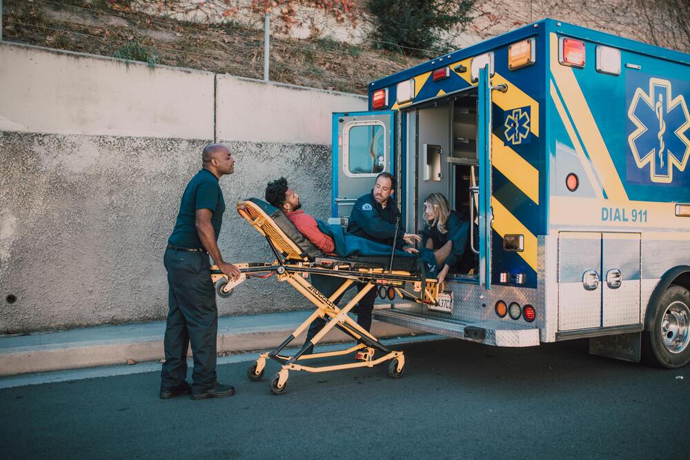 Three EMTs wheeling a person into an emergency vehicle