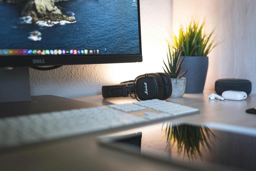 An image of a digital minimalist desk set up. There is a desktop computer, pair of headphones and airpods on a desk.
